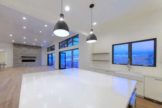 Kitchen island with quartz countertop, pendant lights, and fireplace in background in Deer Mountain custom home, Park City