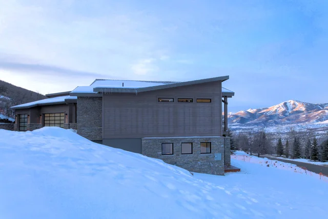 Side exterior of two-story Deer Mountain custom home in deep snow with mountains, Park City