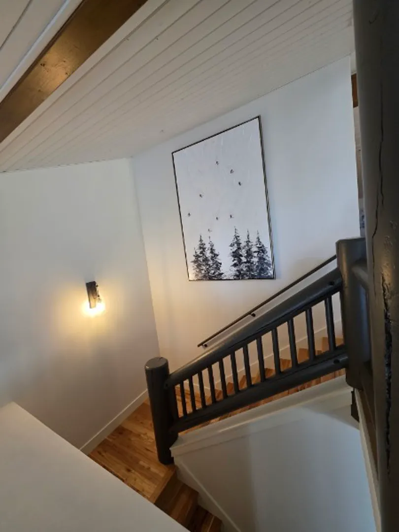 Staircase with dark wood railing, wall sconce, and ski art print in Deer Valley remodel