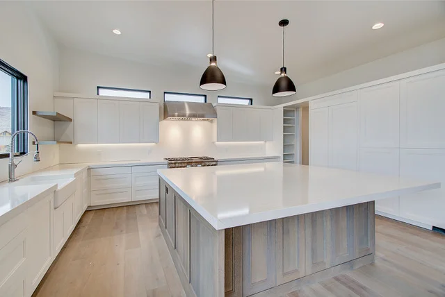 Wide view of kitchen with large island, pendant lights, range hood, and clerestory windows
