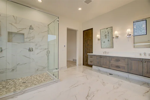 Master bath glass shower with marble walls, dual vanity, and wall sconces in Park City home