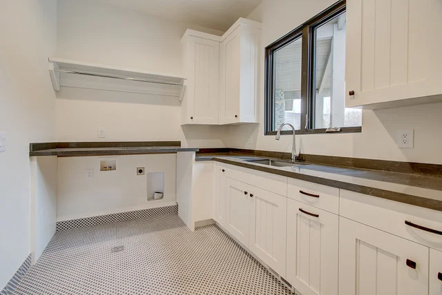 Laundry room with white cabinets, dark wood counter, and penny tile floor in Slalom Run